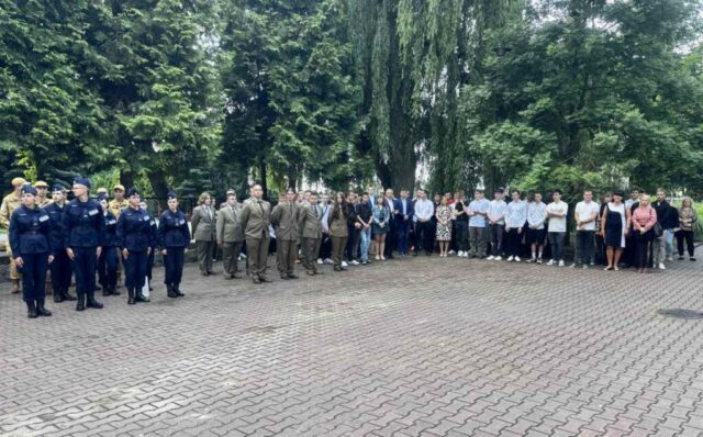 Dziedziniec szkolny, ustawieni w szeregach uczniowie klas Technikum leśnego, OPW oraz pozostałych. W tle drzewa.