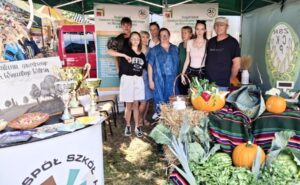 Stoisko ZS CKZ Bujny podczas wystawy Rolszansa. Uczniowie i nauczyciele stoją na stoisku. Stoisko udekorowane warzywami, roślinami, widoczne także banery reklamowe i namiot.