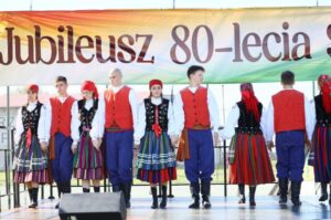 Grupa młodzieży w strojach ludowych na scenie podczas obchodów Jubileuszu 80-lecia Szkoły. W tle baner. 