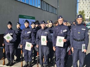 Grupa młodzieży w umundurowaniu i nakryciach głowy przed budynkiem. W tle baner Nadwiślańskiego Oddziału Straży Granicznej. 