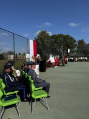 rozpoczecie07 Boisko Szkolne ZS CKZ Bujny, uroczystość rozpoczęcia Roku szkolnego. Po lewej stronie siedzą zaproszeni na uroczystość goście. Widoczna pani Dyrektor przemawiająca do zgromadzonych. Na alszym planie Poczet Sztandarowy oraz uczniowie i nauczyciele.