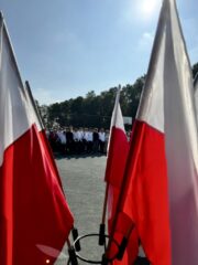 rozpoczecie10 Flagi Polski w stojaki, w tle uczniowie podczas uroczystości Rozpoczęcia Roku Szkolnego w ZS CKZ Bujny na terenie Orlika.