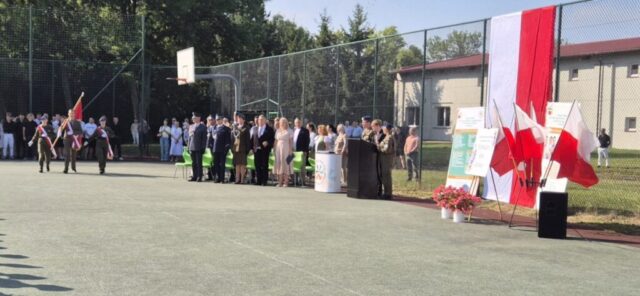 Boisko Szkolne ZS CKZ Bujny, uroczystość rozpoczęcia Roku szkolnego. Poczet Sztandarowy, zaproszeni goście, Dyrekcja Szkoły oraz uczniowie i rodzice. Stojak z flagami Polski, rollupy promocyjne Szkoły.