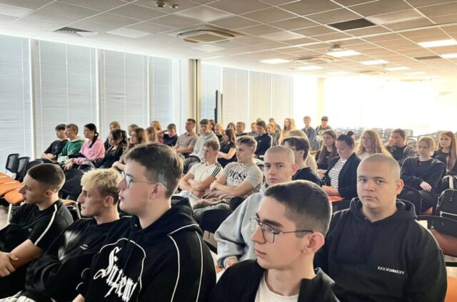Uczniowie i wychowawcy siedzą w dużej, jasnej auli.
