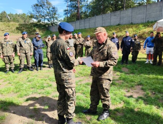 Uczeń klasy mundurowej odbiera dyplom z rąk organizatora zawodów strzeleckich.