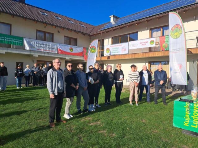 Grupa osób na dziedzińcu, w otoczeniu budynków. Na balkonach banery LZS, Ministerstwa Sportu i Turystyki.