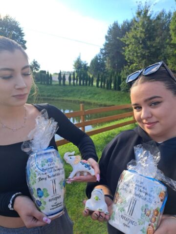 Uczestniczki zlotu prezentują zdobyte nagrody. W tle staw ogrodzony płotem drewnianym i zieleń.