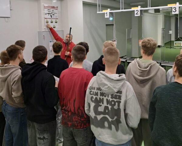 Grupa młodzieży wraz z instruktorem wewnątrz strzelnicy.