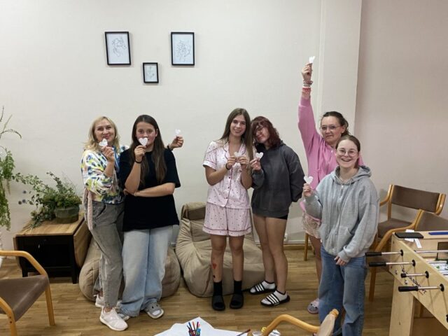 Grupa uczennic wraz z osobą dorosłą w pomieszczeniu. Trzymają w rękach wycięte z papieru białe serduszka.