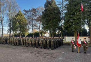 apel_odzyskanie_niepodleglosci08 Uczniowie w umundurowaniu i poczet sztandarowy na dziedzińcu szkoły podczas apelu.