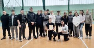 Grupa młodzieży w hali sportowej. Dwie osoby w trzymają w rękach.