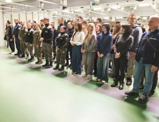 Młodzież oraz opiekunowie wewnątrz sali. Część młodzieży w umundurowaniu.