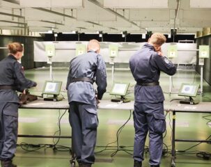 zawody_strzeleckie03 3 osoby w umundurowaniu wewnątrz strzelnicy przy stanowiskach, oddają strzały.