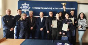 Zwycięska drużyna wraz z opiekunem i organizatorami turnieju. W tle baner reklamowy Komendy Miejskiej Policji w Piotrkowie Trybunalskim.