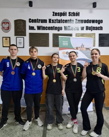 Pięcioro uczniów w strojach sportowych stoi w rzędzie, prezentując medale zdobyte podczas szkolnych zawodów.