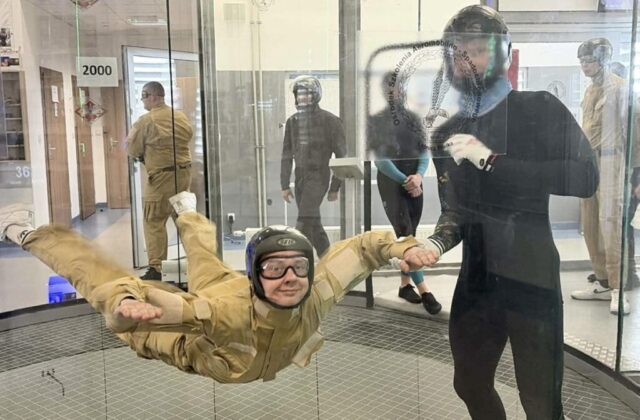 Instruktor pomaga uczestnikowi utrzymać pozycję w tunelu aerodynamicznym.