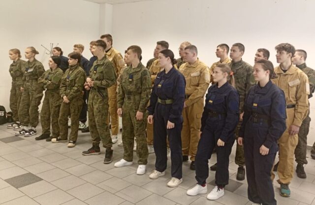 Kadeci klas OPW w różnych mundurach stoją w rzędach w pomieszczeniu, jak podczas odprawy lub instruktażu.