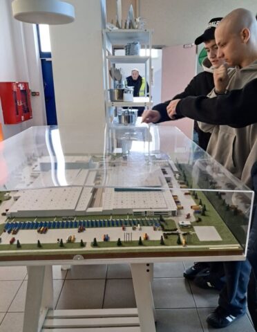 Dwie osoby wskazują elementy makiety przedstawiającej obiekt przemysłowy.