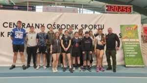 Grupa młodzieży w strojach sportowych wraz z opiekunem podczas wydarzenia sportowego po ceremonii dekorowania medalami. 