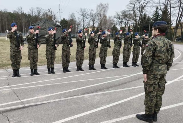 Kadeci klasy OPW podczas prezentacji broni. Przed nimi stoi dowódca. W tle namiot wojskowy.