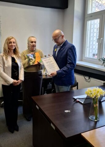 Trzy osoby prezentują książkę i dokument w sali wykładowej.