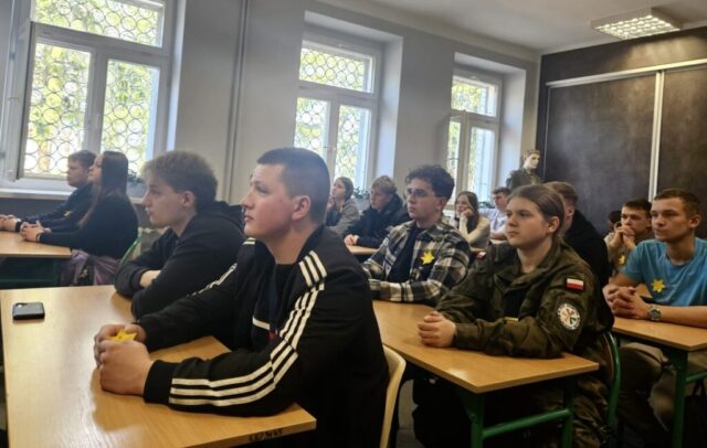 Uczniowie siedzą w sali wykładowej, słuchając zajęć