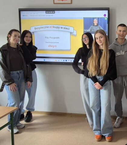 Pięcioro uczniów stoi przed ekranem z prezentacją o bezpiecznych zakupach w sieci.