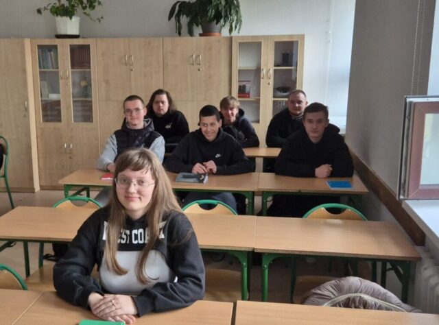 Uczniowie siedzą w ławkach w klasie podczas zajęć.