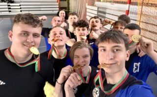 pilka_nozna_halowa01 Szkolna drużyna w strojach sportowych prezentuje zdobyte medale. Widoczny też opiekun.