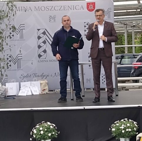 moszczenica2 Dwie osoby stoją na scenie podczas wydarzenia plenerowego, jedna przemawia do mikrofonu.