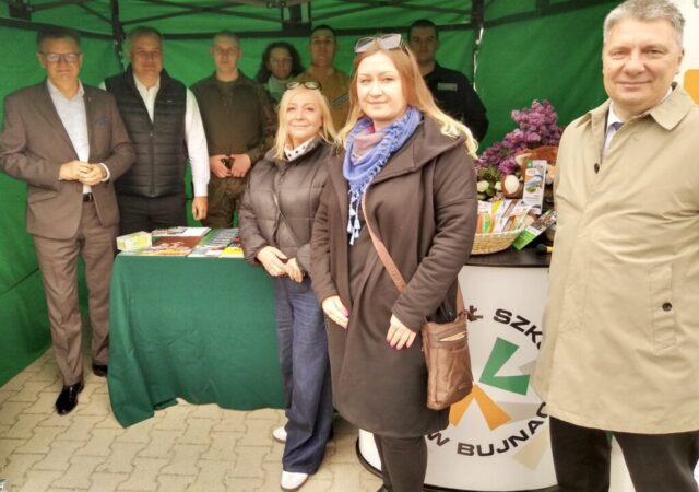moszczenica4 Grupa osób pod zielonym namiotem prezentuje materiały informacyjne na szkolnym stoisku.