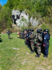 oboz_zloty_potok02 Odprawa przy ścianie skalnej — grupa w kaskach i uprzężach stoi w szyku przed skałą podczas szkolenia wspinaczkowego.