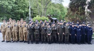 oboz_zloty_potok19 Zdjęcie grupowe przy pomniku — duża grupa w różnych mundurach stoi przed pomnikiem jelenia.