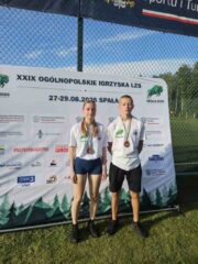 Igrzyska_LZS_final_centralny2 Dwoje zawodników z brązowymi medalami stoi przed banerem ogólnopolskich igrzysk LZS.