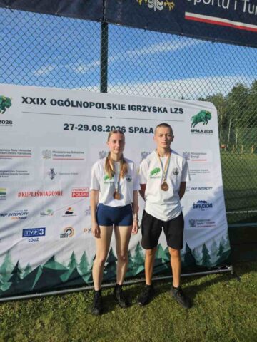 Igrzyska_LZS_final_centralny2 Dwoje zawodników z brązowymi medalami stoi przed banerem ogólnopolskich igrzysk LZS.