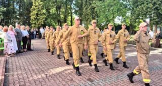 Rozpoczecie_roku_szkolnego8 Grupa osób w jasnych mundurach maszeruje w szyku, mijając obserwatorów.