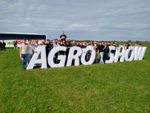 Grupa uczniów wraz z opiekunami stojąca na terenie wystawy, pozująca przy dużym napisie „AGRO SHOW”.