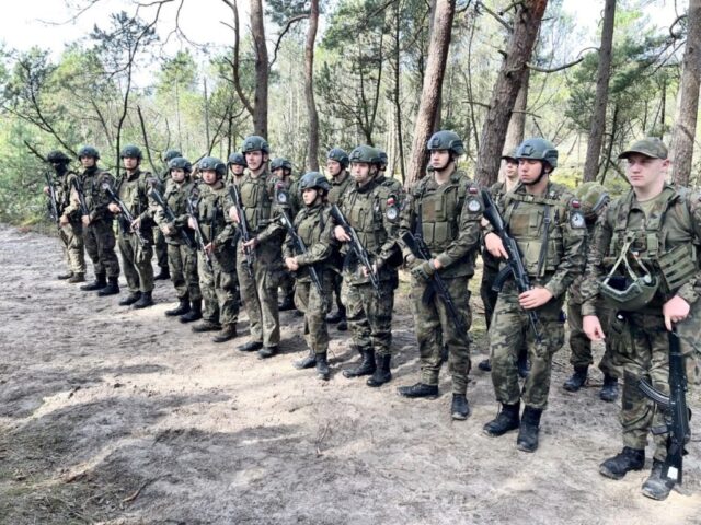 Uczniowie stoją w lesie podczas ćwiczeń wojskowych.