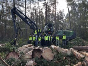 Uczniowie na powierzchni zrębowej przy maszynie leśnej typu harvester