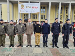 Uczniowie w umundurowaniu podczas wydarzenia plenerowego przed budynkiem targowym.