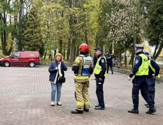 Funkcjonariusze służb mundurowych i pani wicedyrektor przed budynkiem szkoły podczas ćwiczeń ewakuacyjnych.