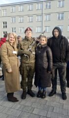 Osoba w mundurze wojskowym oraz trzy osoby podczas uroczystości wojskowej.
