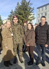 Osoba w mundurze wojskowym i trzy osoby pozujące do wspólnego zdjęcia na terenie jednostki wojskowej.